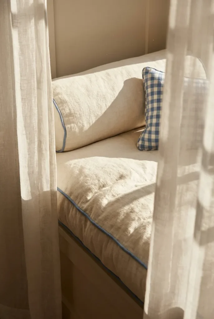 Coastal window seat cushion in white linen with blue piping and a gingham lumbar pillow.