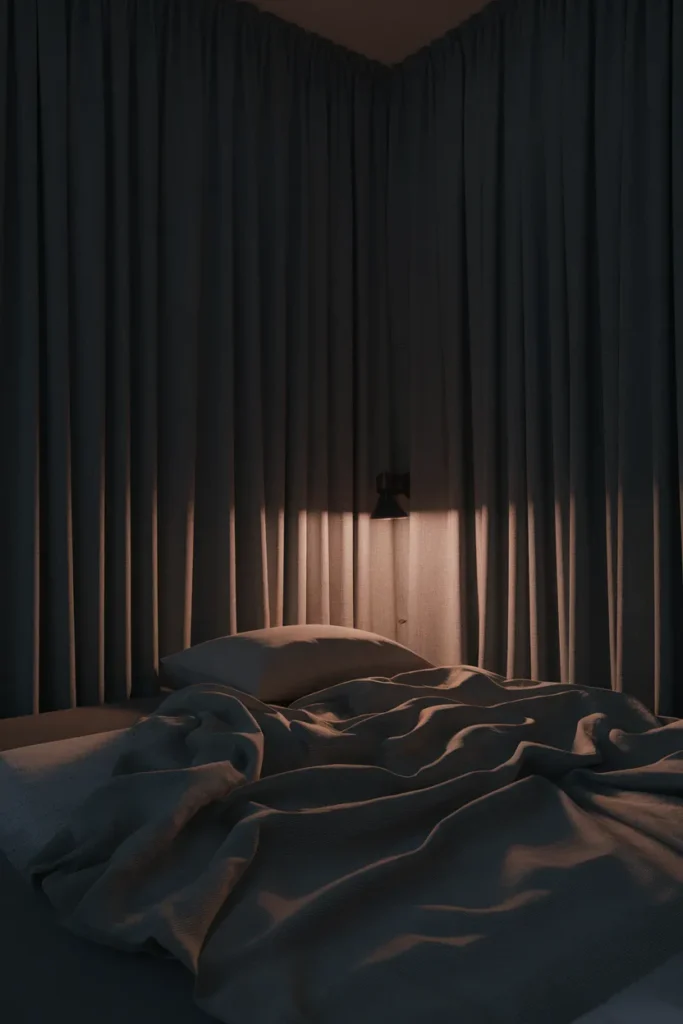 Blackout curtains drawn at night in a dark, cool, cozy bedroom for better sleep.
