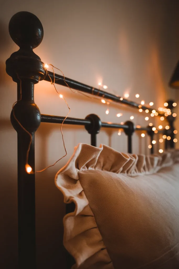 Close-up of warm copper wire fairy lights woven along a black iron bed headboard.