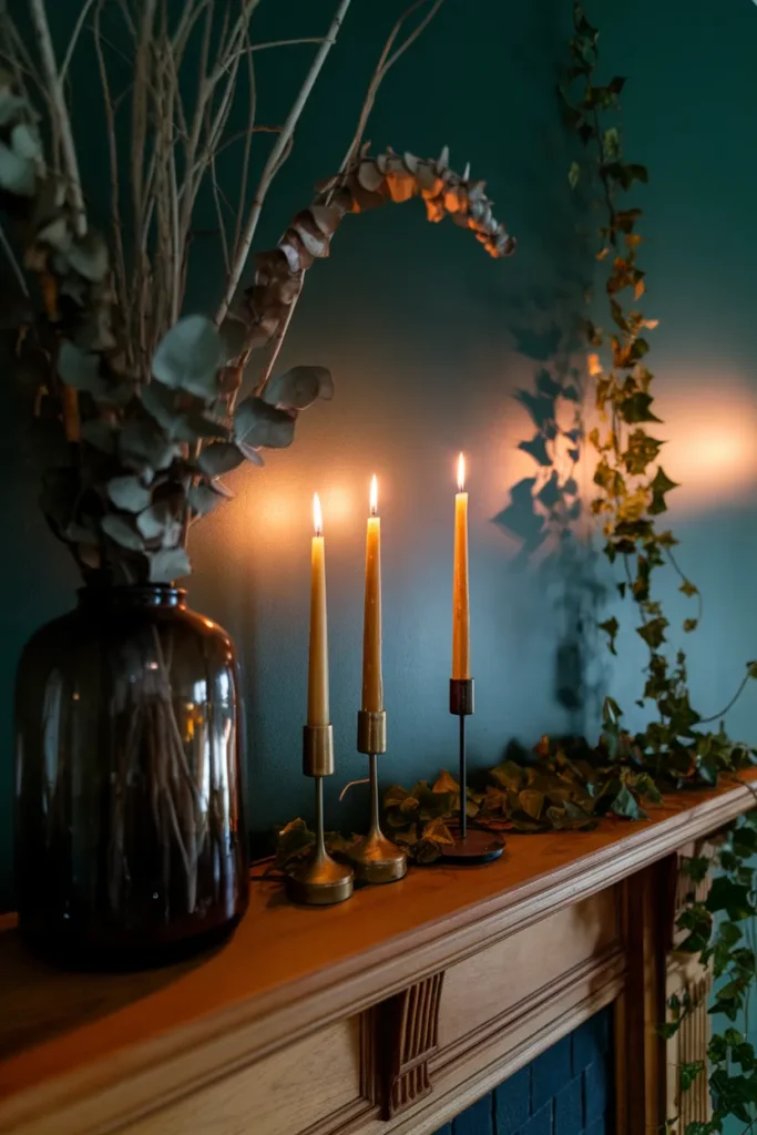 Dried branches and lit taper candles on a mantel in a dark cottagecore aesthetic living room.