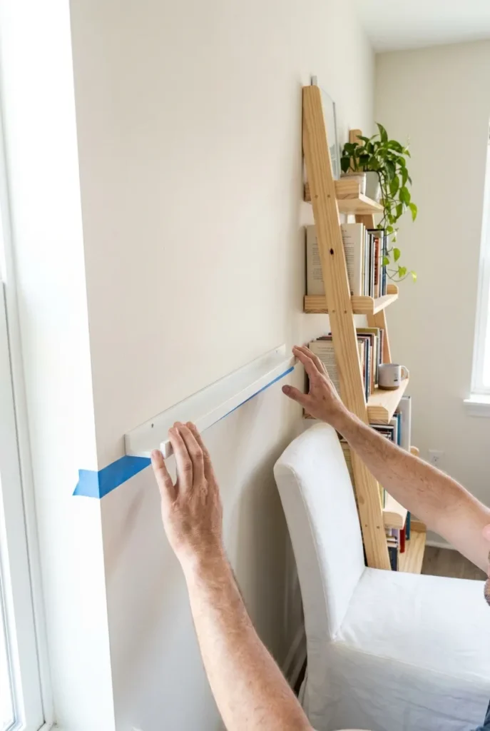 Hands mounting a no-drill adhesive book ledge next to a leaning ladder shelf.