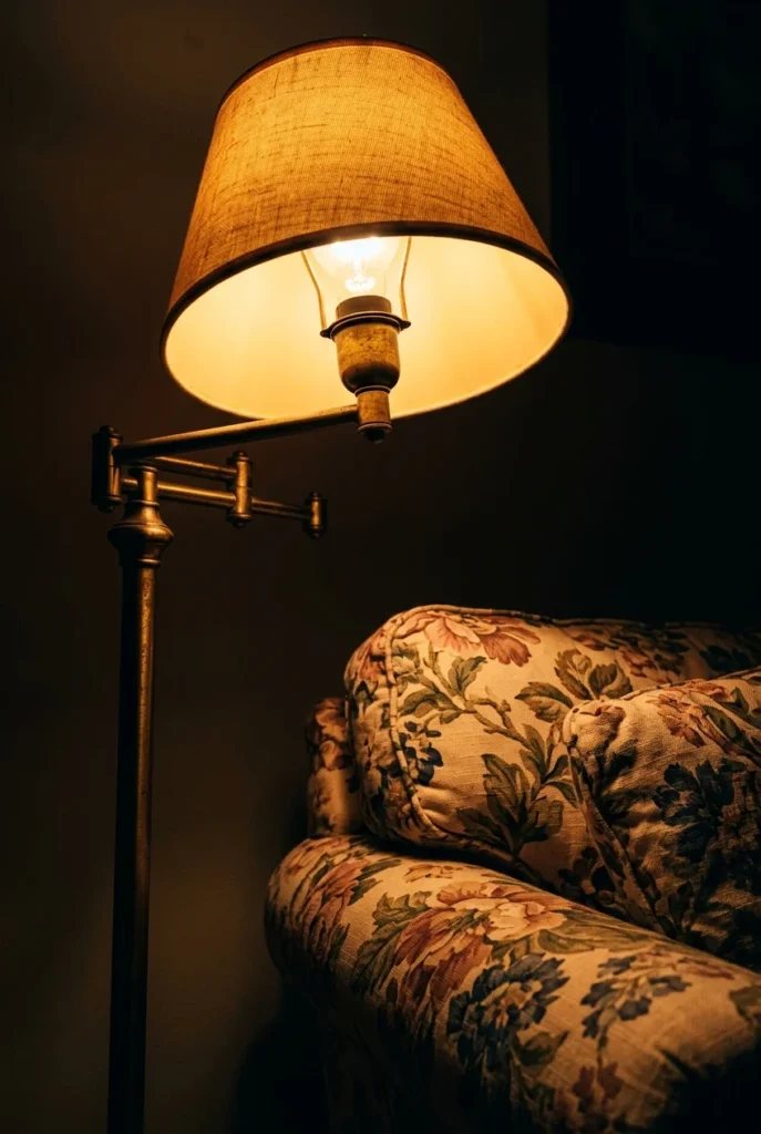 Brass swing-arm lamp glowing warm 2700K light across a floral sofa at night.