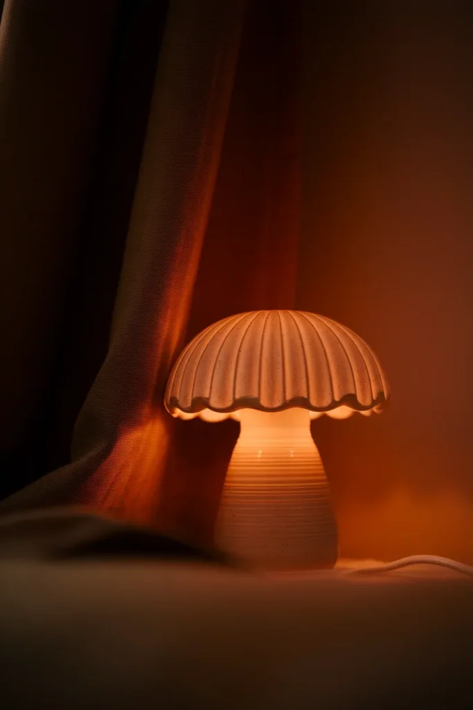 Ceramic mushroom lamp with scalloped shade glowing warm in a dim whimsical bedroom.