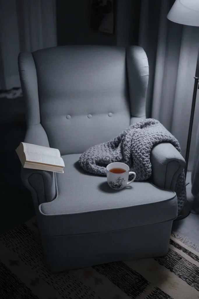 Empty armchair at night with an open paperback, half-finished tea and a wool throw sliding off.