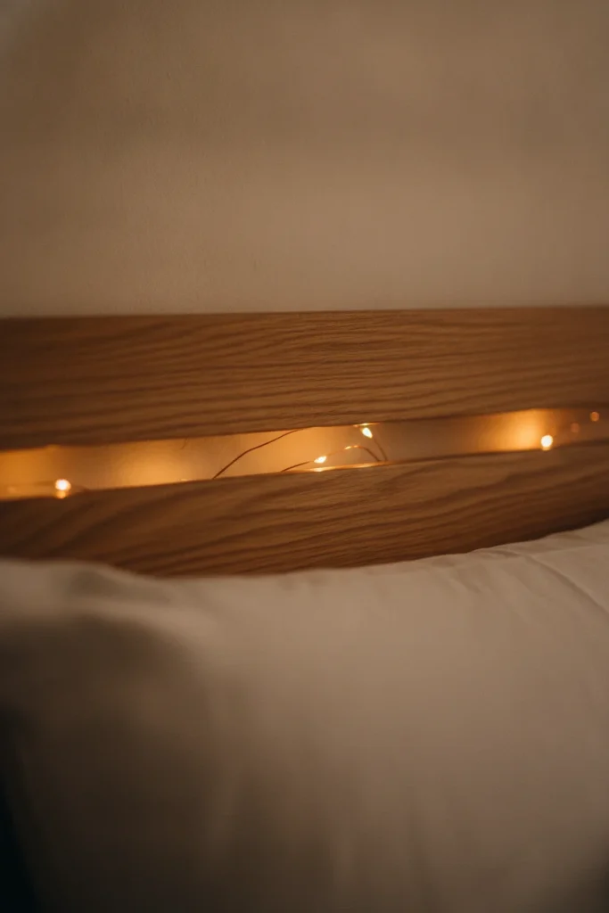 Fairy lights hidden behind a wooden headboard casting a soft amber halo up a cream wall.