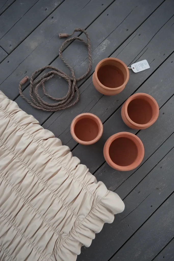 Flat lay of cottagecore patio starter supplies cream cushion, string lights, and three terracotta pots.