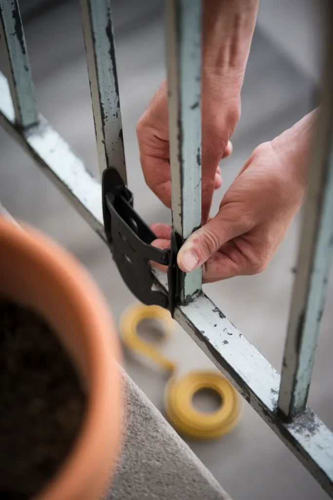 Hands clamping an over-rail planter bracket onto a balcony railing with a tape measure nearby.