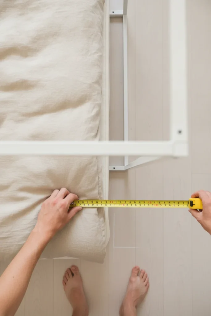 Hands measuring 12 inches out from a mattress edge to mark canopy rail placement.