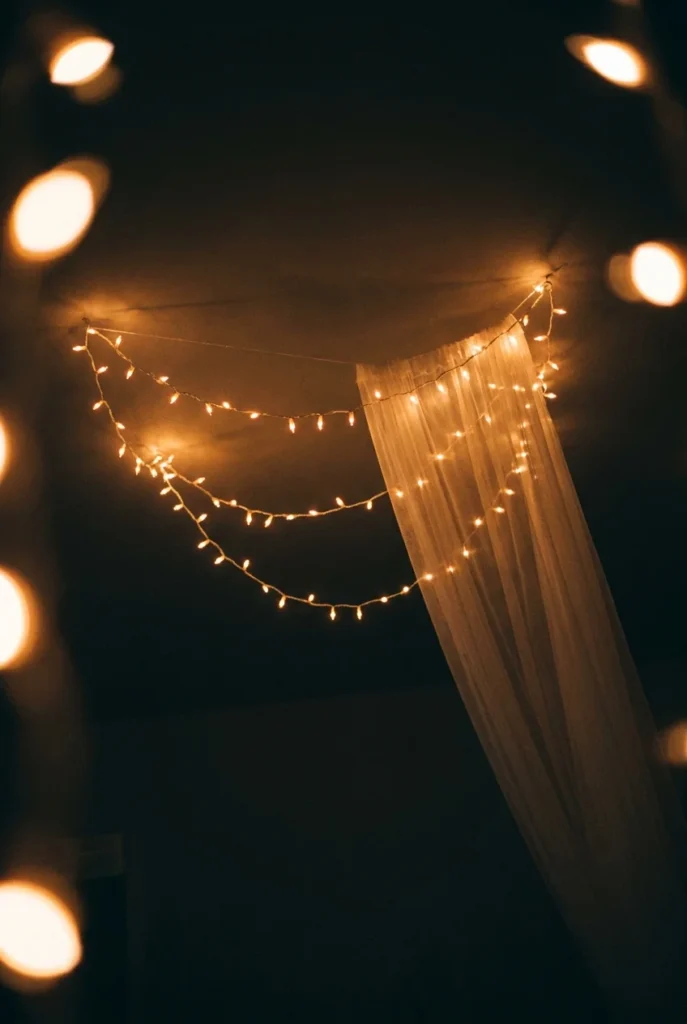 Looking up at a fairy light canopy over a bed at night with sheer fabric draped across the strings.