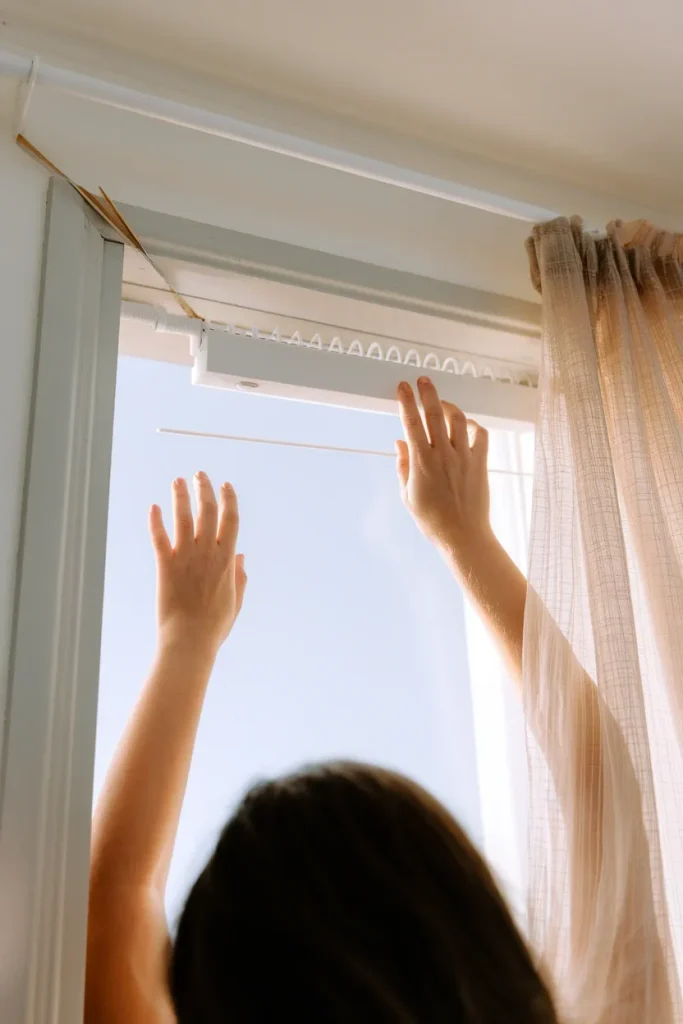 Over the shoulder view of hands installing a no-drill tension rod inside a rental window frame.