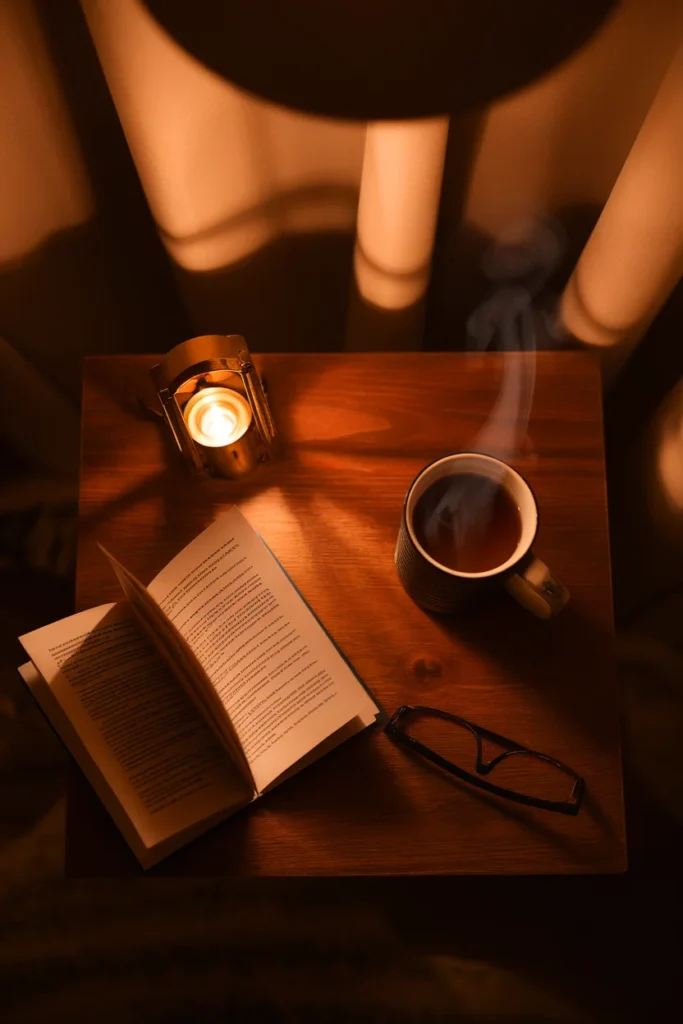 Overhead night view of a balcony table with an open book, tea, glasses and a lantern.