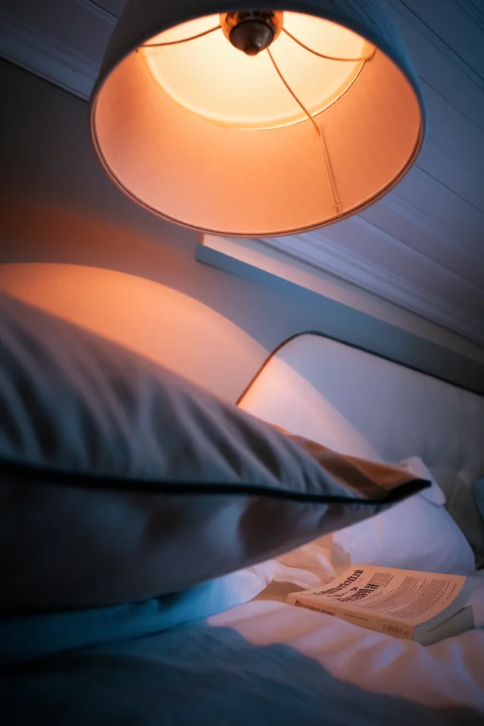 View from a pillow looking up at a warm bedside lamp shade glowing against a dark ceiling.