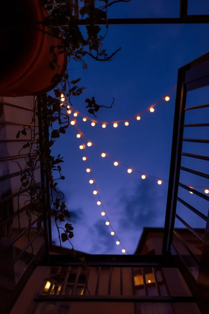Warm string lights swagged across a deep blue dusk sky above a balcony, seen from below.