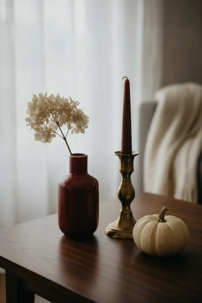 Oxblood vase, brass taper holder, and cream pumpkin on a walnut coffee table in a fall 2026 color palette