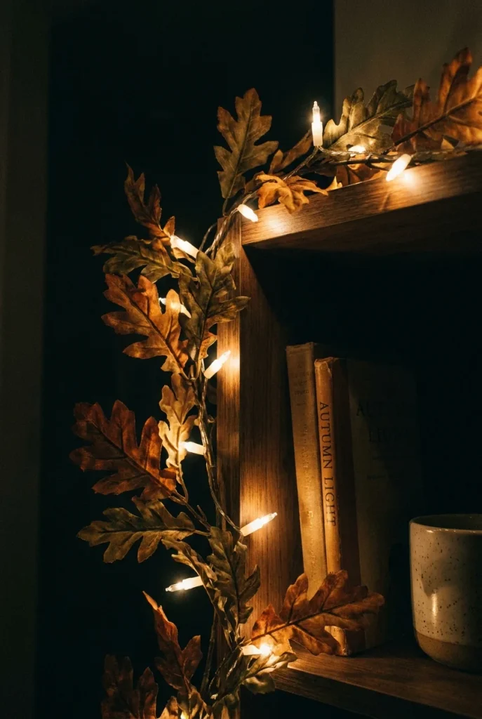 Warm fairy lights beside a fall leaf garland on a shelf edge at night.