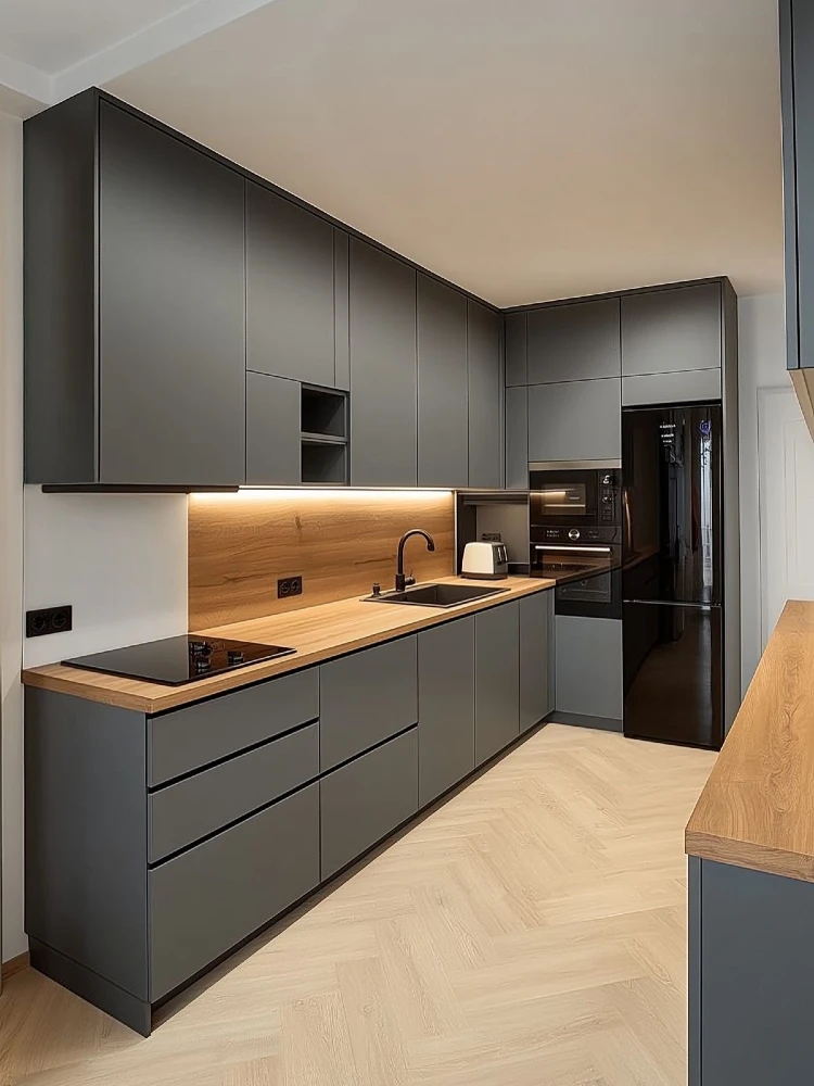 Sleek modern kitchen with matte grey handleless cabinetry, a light wood countertop and backsplash, under-cabinet lighting, a black induction cooktop, a black built-in fridge and oven, and herringbone-patterned flooring.