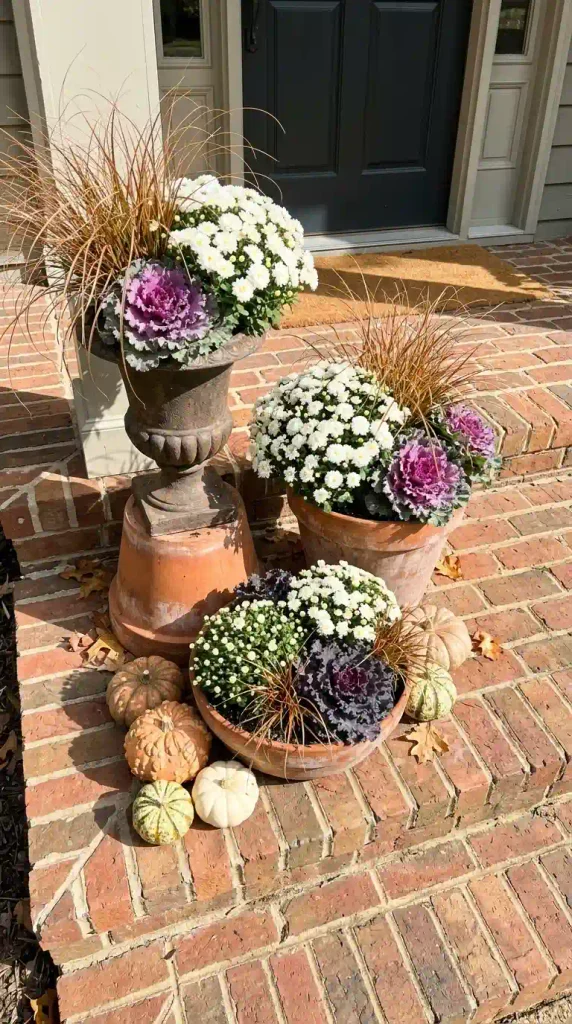 Three fall porch planters grouped at staggered heights on a brick stoop