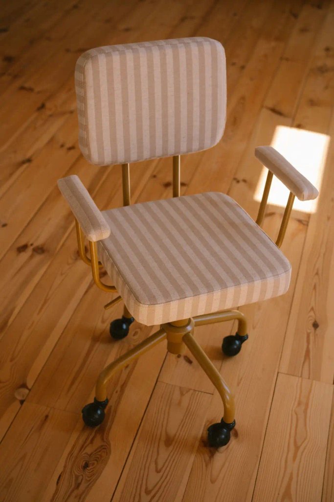 A vintage swivel office desk chair with beige and white striped fabric upholstery